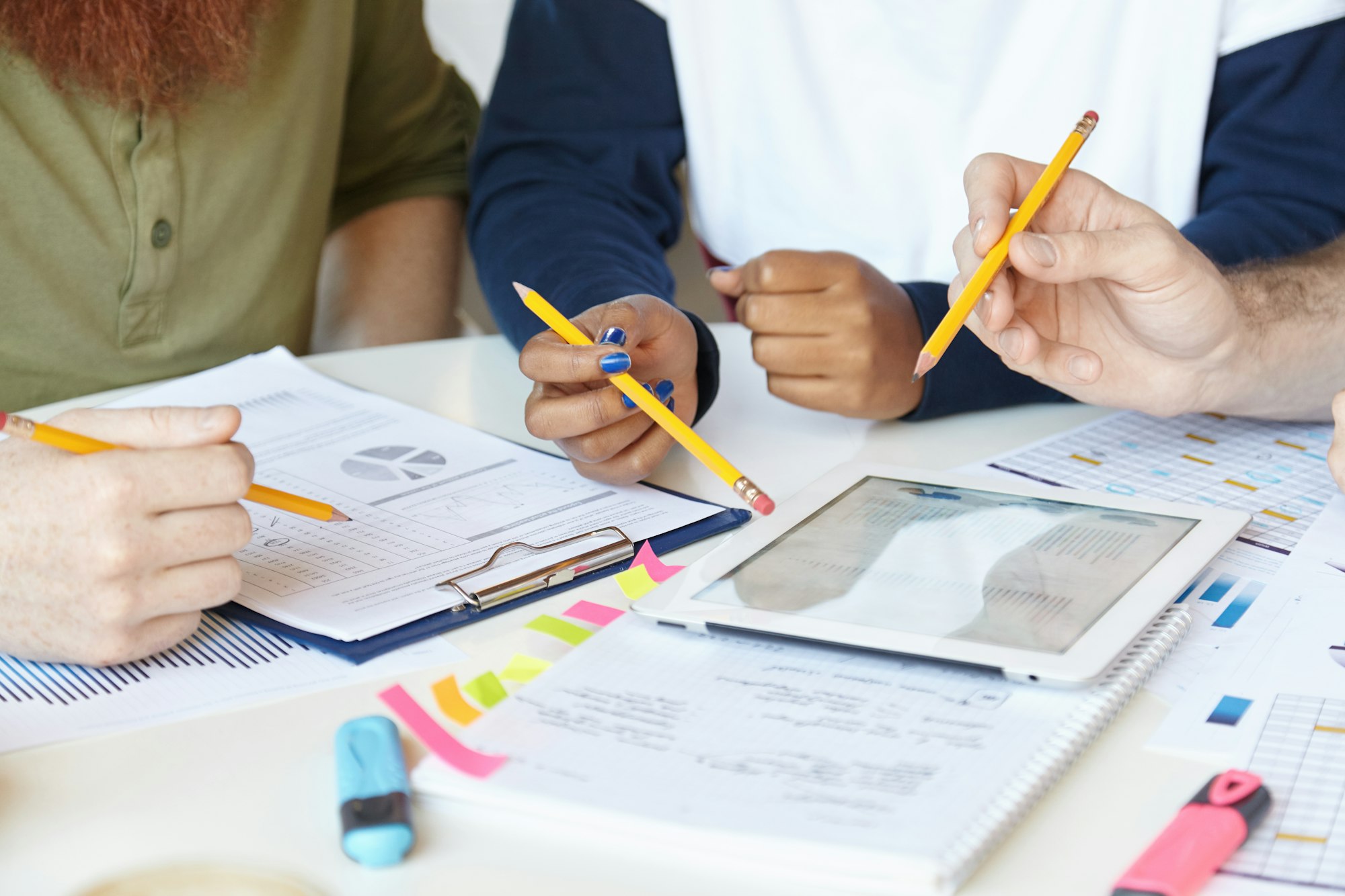 Team of creative young people holding pencils while discussing business strategy and plans of their