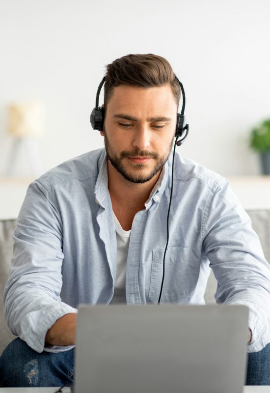 Hotline support service. Millennial male call center operator in headset working with laptop at home